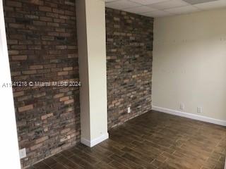 An empty room features a brick accent wall, a central pillar, and wood-look tile flooring — 13499 Biscayne Blvd, North Miami FL 33181, NORTH MIAMI, FL