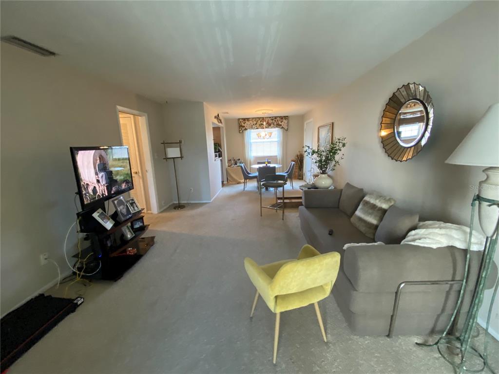 A living room with beige carpet, a gray sofa, a yellow chair, and a dining area — 1500 GAY ROAD UNIT 4D, WINTER PARK, FL