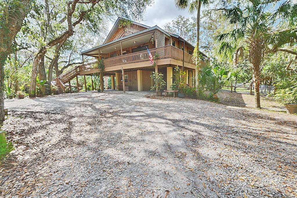 A two-story house with a wooden deck and staircase sits on a gravel lot — 6618 S BEAGLE DRIVE, HOMOSASSA, FL