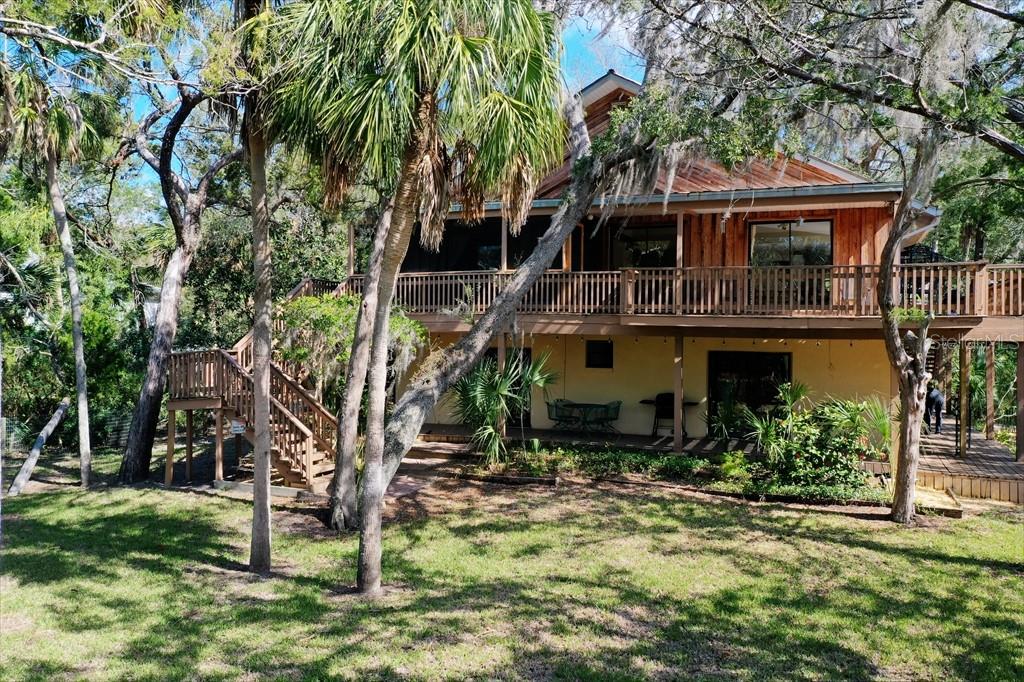 A two-story wooden house features a large wrap-around deck and a ground-level patio area — 6618 S BEAGLE DRIVE, HOMOSASSA, FL
