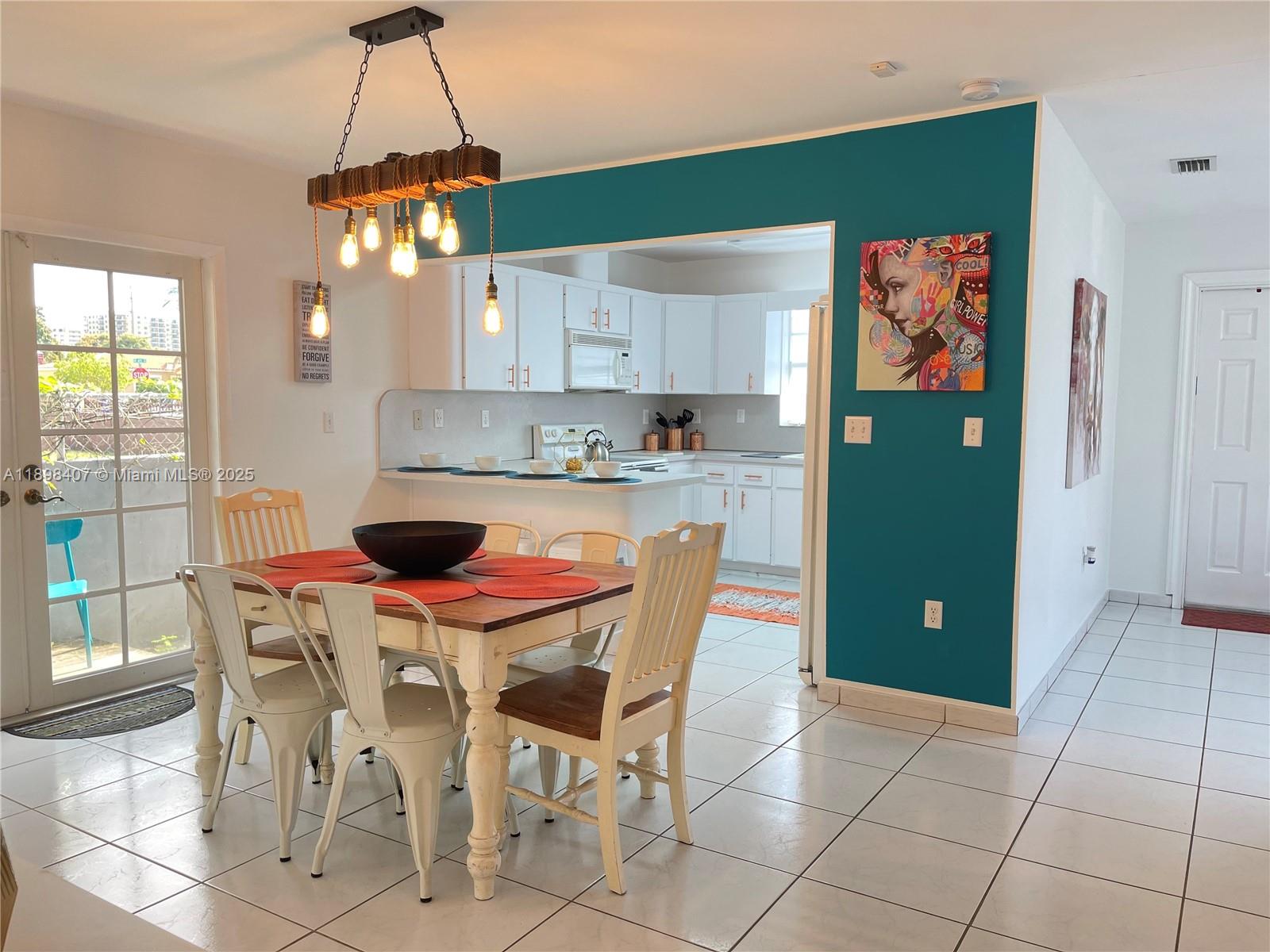 A dining area with a wooden table and pendant light opens into a white kitchen — 4521 NW 4th St # 4521, Miami FL 33126, MIAMI, FL