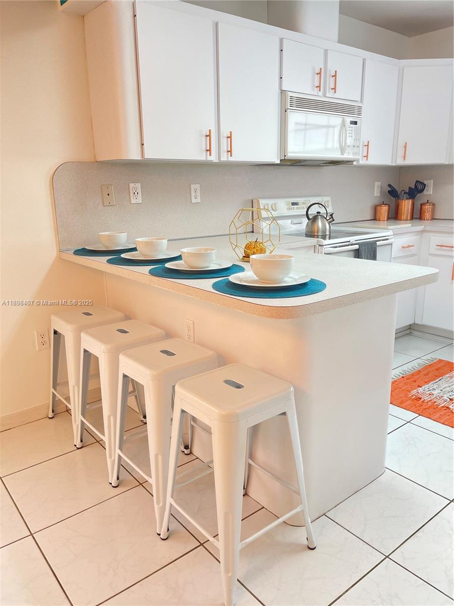 A kitchen features a white breakfast bar with four stools and white cabinetry — 4521 NW 4th St # 4521, Miami FL 33126, MIAMI, FL