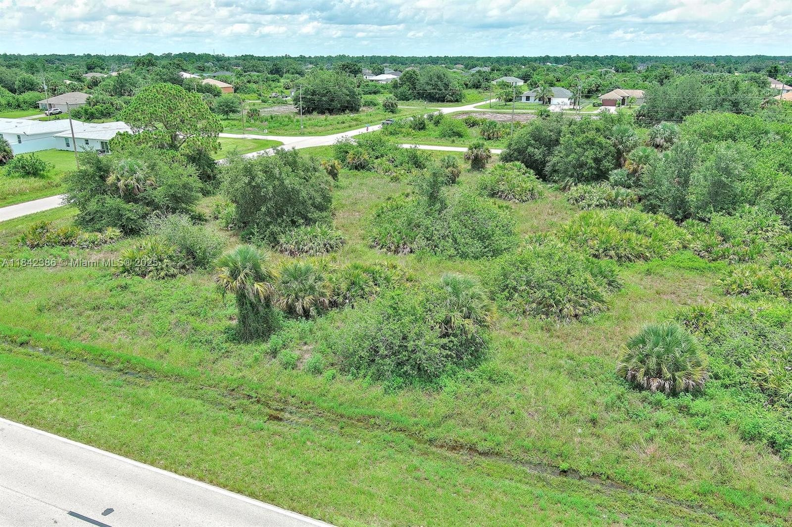An aerial view shows a vacant, overgrown lot with scattered trees and shrubs near residential houses — 841 Milwaukee Blvd, Lehigh Acres FL 33974, LEHIGH ACRES, FL