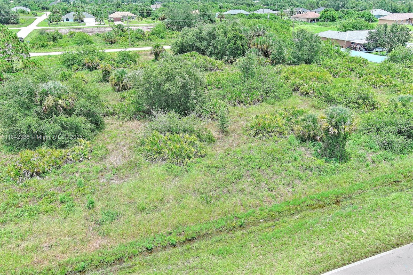 An aerial view shows a vacant, grassy lot with scattered trees and shrubs in a residential area — 841 Milwaukee Blvd, Lehigh Acres FL 33974, LEHIGH ACRES, FL
