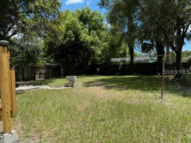 A grassy backyard features a wooden fence, mature trees, and a clothesline pole — 1410 W HUMPHREY STREET, TAMPA, FL