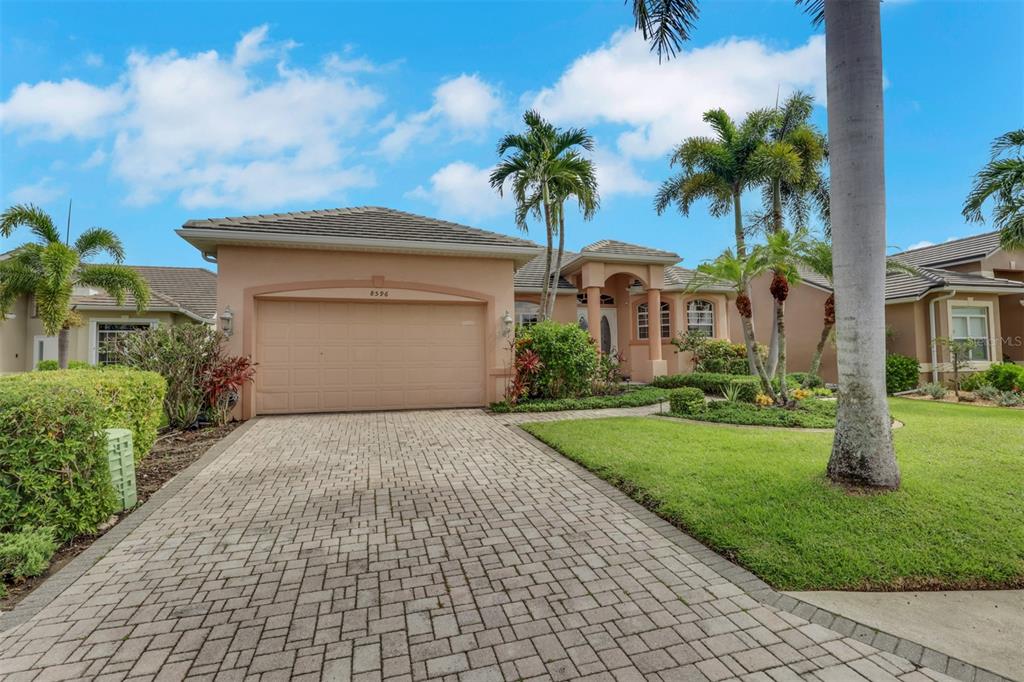 A single-story house with a beige stucco exterior, a paved driveway, and several palm trees — 8596 SOUTHWIND BAY CIRCLE, FORT MYERS, FL
