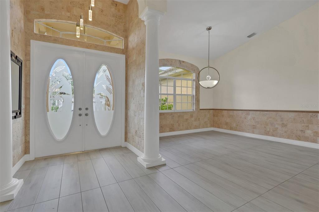 A bright entryway features a double door, stone-tiled walls, a white column, and gray flooring — 8596 SOUTHWIND BAY CIRCLE, FORT MYERS, FL
