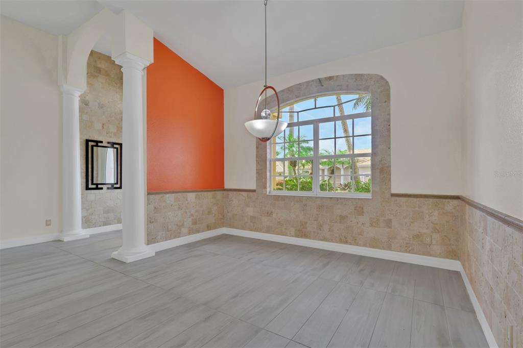 A dining room features gray wood-look flooring, stone wainscoting, an orange accent wall, and columns — 8596 SOUTHWIND BAY CIRCLE, FORT MYERS, FL