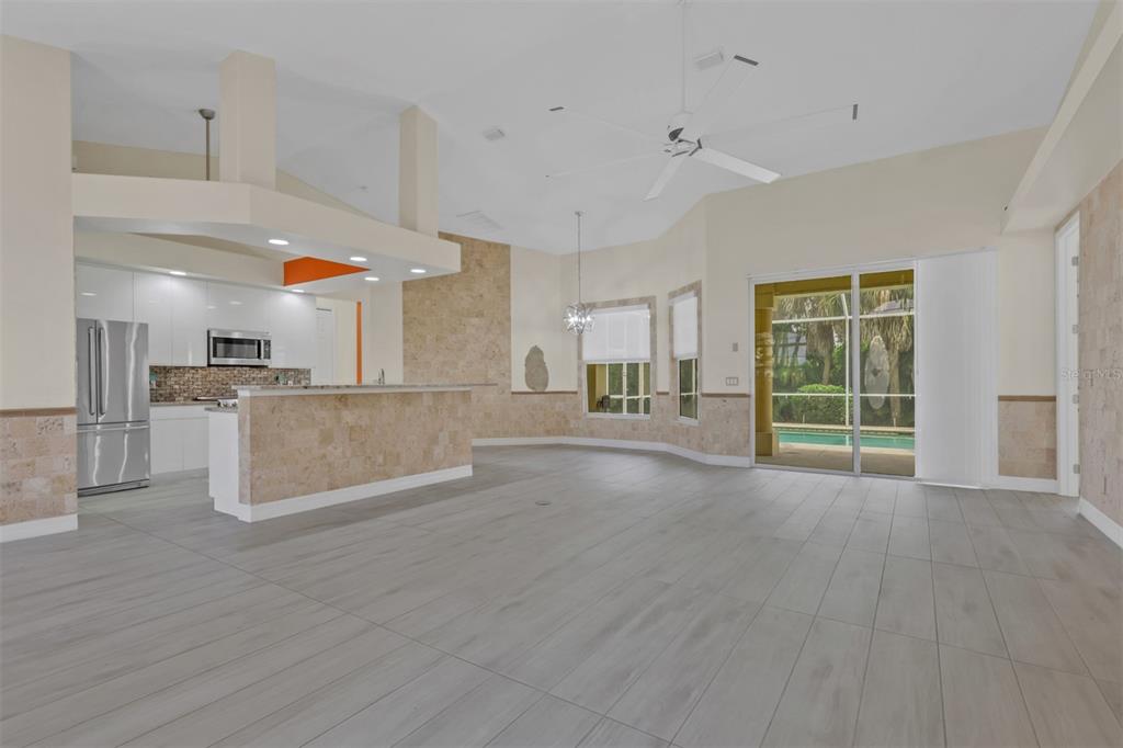 An open-concept kitchen and living area with tile flooring, stone accents, and sliding glass doors — 8596 SOUTHWIND BAY CIRCLE, FORT MYERS, FL