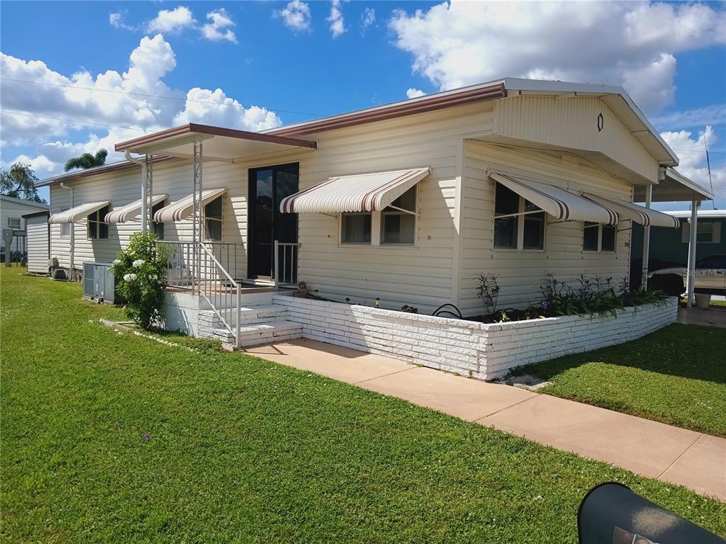 A single-story mobile home with light siding, striped window awnings, and a white brick planter — 5229 BEL AIR AVENUE, SARASOTA, FL