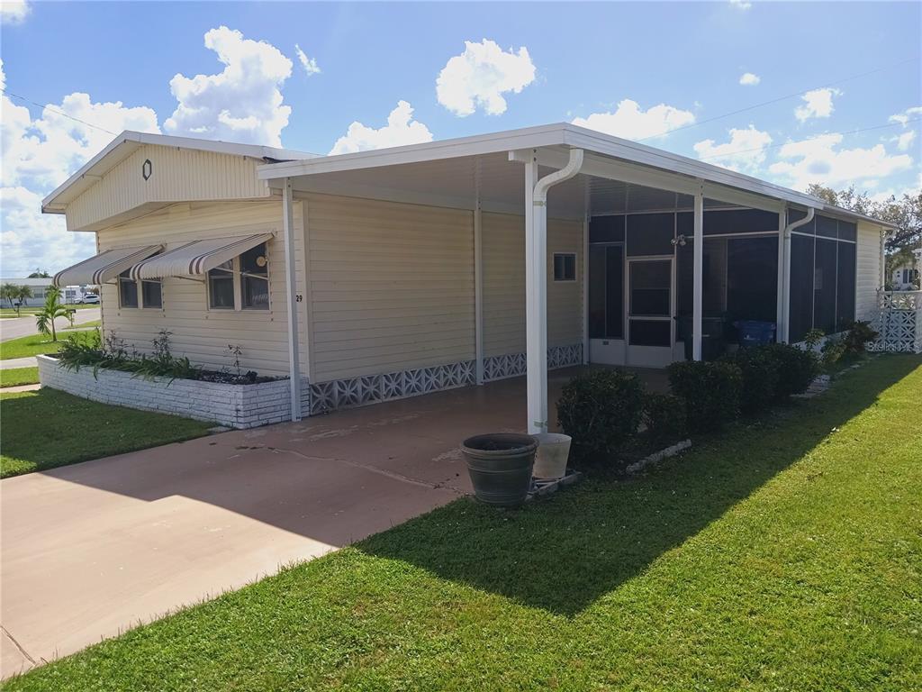A single-story mobile home with a carport, screened porch, and white brick planter — 5229 BEL AIR AVENUE, SARASOTA, FL