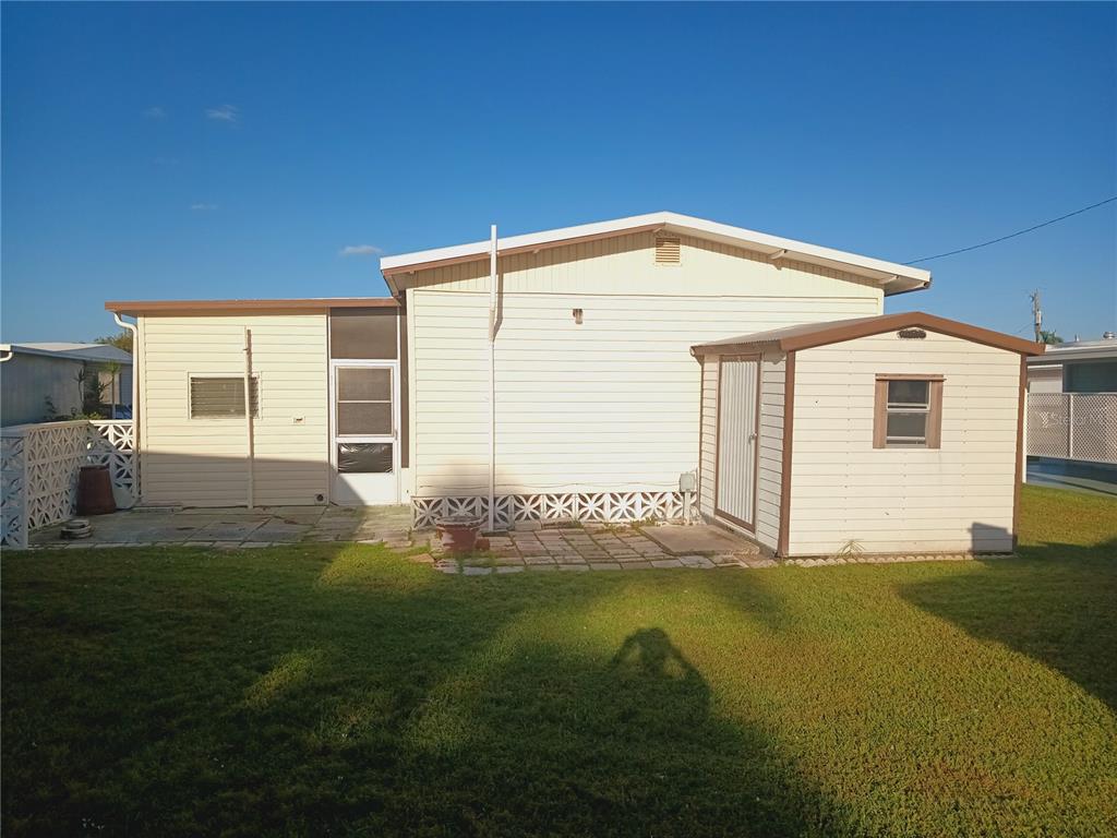 The exterior of a light-colored mobile home features a small attached shed and a patio — 5229 BEL AIR AVENUE, SARASOTA, FL