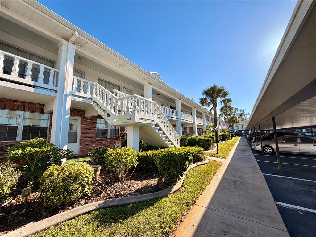 Exterior view of a two-story apartment building with a white staircase and covered parking — 4747 AZALEA DRIVE UNIT 231, NEW PORT RICHEY, FL