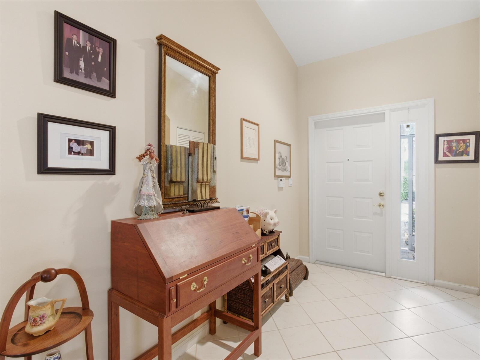 An entryway features a wooden secretary desk, a mirror, framed photos, and white tile flooring — 9624 Crescent View Drive N, Boynton Beach FL 33437, BOYNTON BEACH, FL