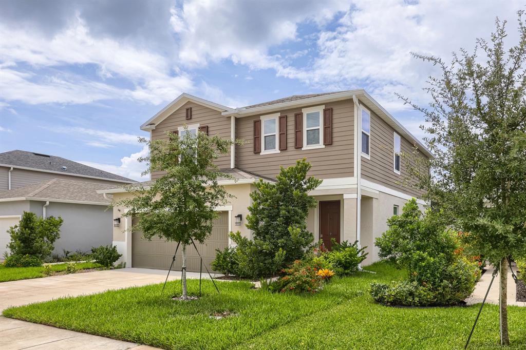A two-story suburban house with tan siding, a two-car garage, and a landscaped front yard — 37434 YUKON DRIVE, ZEPHYRHILLS, FL