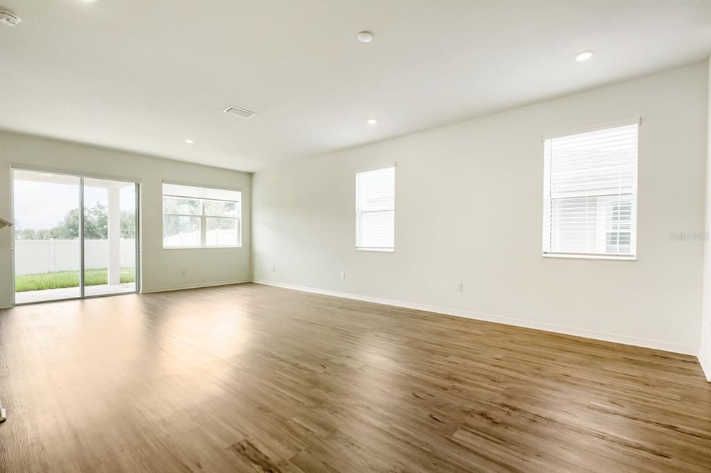 An empty living room features light wood-look flooring, white walls, recessed lighting, and sliding doors — 37434 YUKON DRIVE, ZEPHYRHILLS, FL