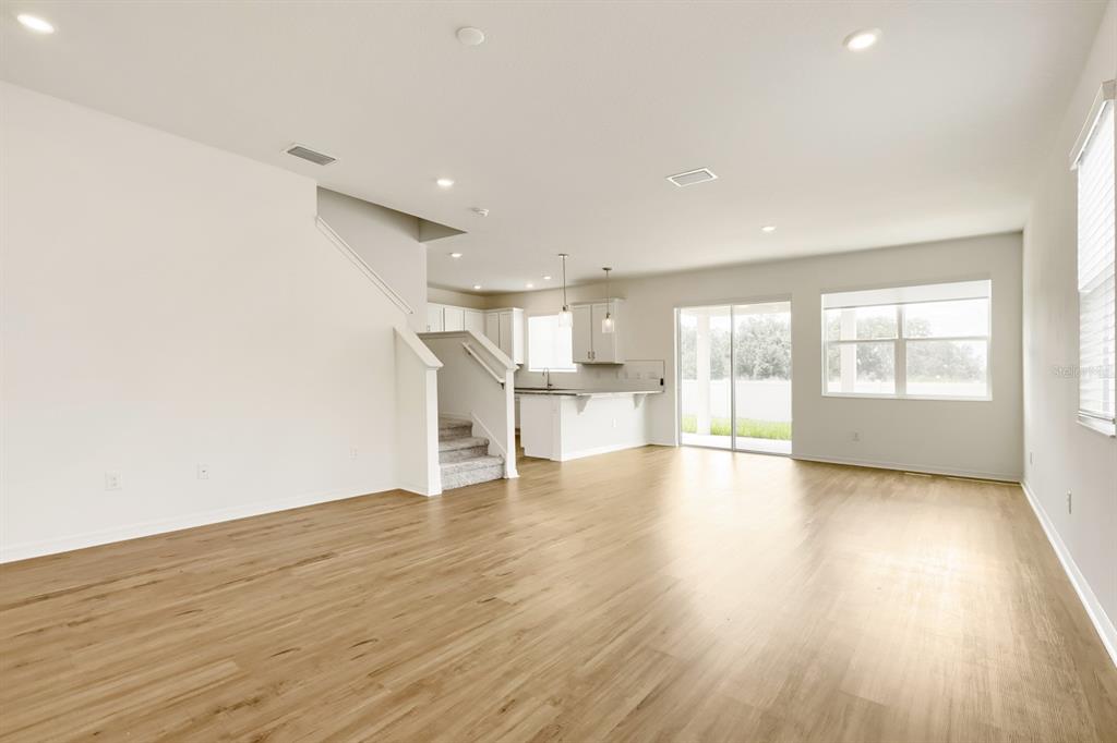An open-concept living area with light wood-look flooring, a staircase, and a kitchen in back — 37434 YUKON DRIVE, ZEPHYRHILLS, FL
