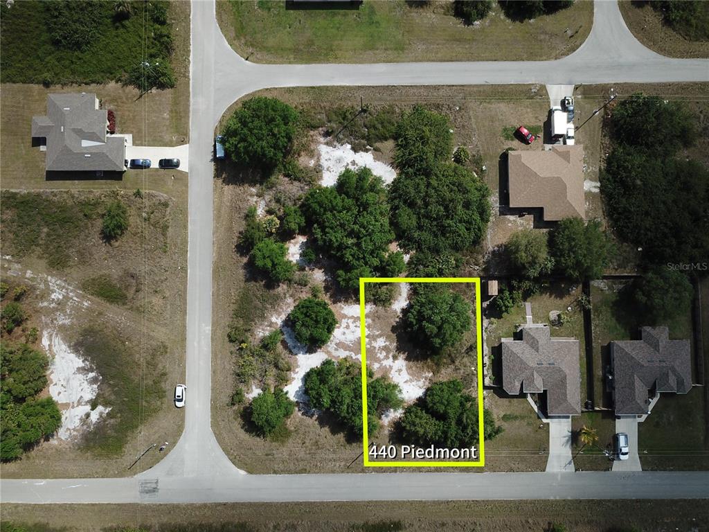 This aerial view shows a vacant, partially wooded residential lot outlined in yellow — 440 PIEDMONT STREET, LEHIGH ACRES, FL