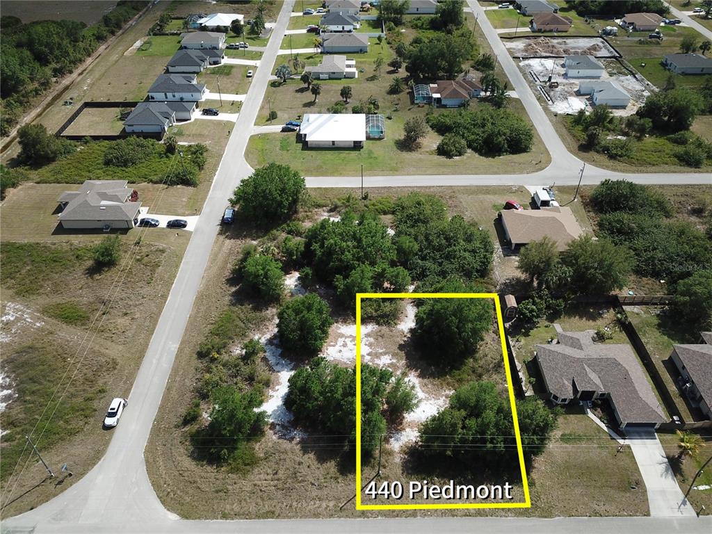 An aerial view shows a vacant, tree-covered residential lot outlined in yellow — 440 PIEDMONT STREET, LEHIGH ACRES, FL