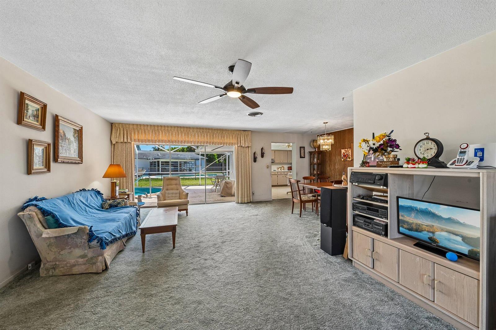 A living room with carpeted floors, a ceiling fan, and a sliding door to a pool — 804 SE 16th Court, Deerfield Beach FL 33441, DEERFIELD BEACH, FL