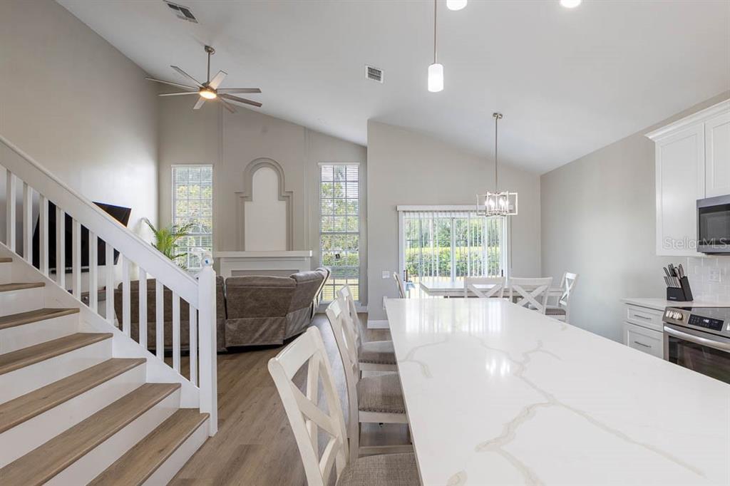 A kitchen island with a quartz countertop overlooks a living room with stairs and windows — 3432 IDLEGROVE COURT, ORLANDO, FL