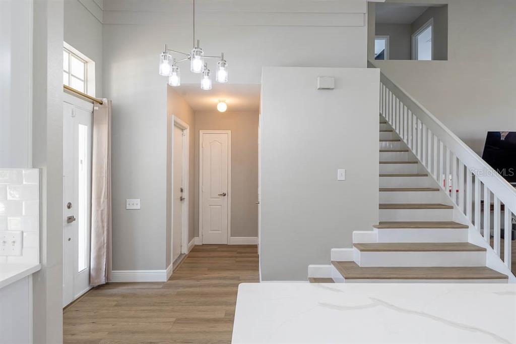 A bright entryway features light wood flooring, a white staircase, and a modern chandelier — 3432 IDLEGROVE COURT, ORLANDO, FL