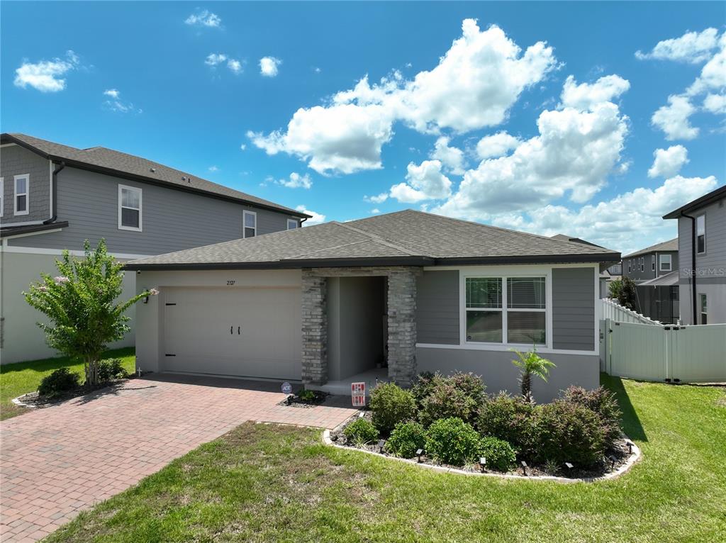 A single-story house with a gray exterior, stone accents, a two-car garage, and a driveway — 2327 BEAR PEAK ROAD, MINNEOLA, FL