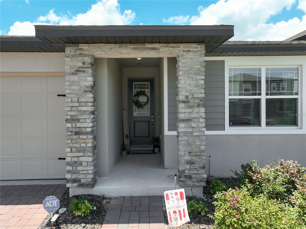 The exterior of a house features a stone-accented entryway, a gray front door, and a garage — 2327 BEAR PEAK ROAD, MINNEOLA, FL