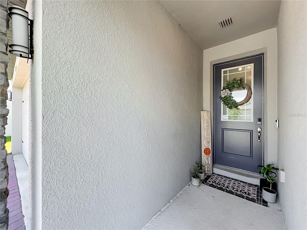 A gray front door with a wreath and a welcome sign sits on a porch — 2327 BEAR PEAK ROAD, MINNEOLA, FL