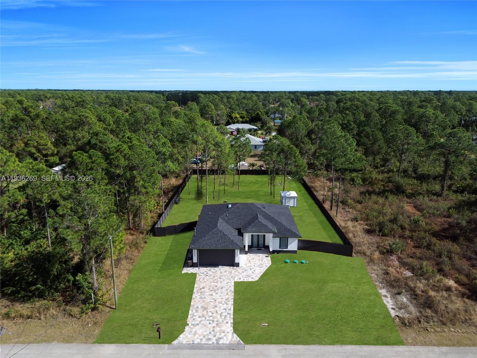 An aerial view shows a modern house with a paved driveway surrounded by a large yard — 1112 Clark Ave, Lehigh Acres FL 33972, LEHIGH ACRES, FL