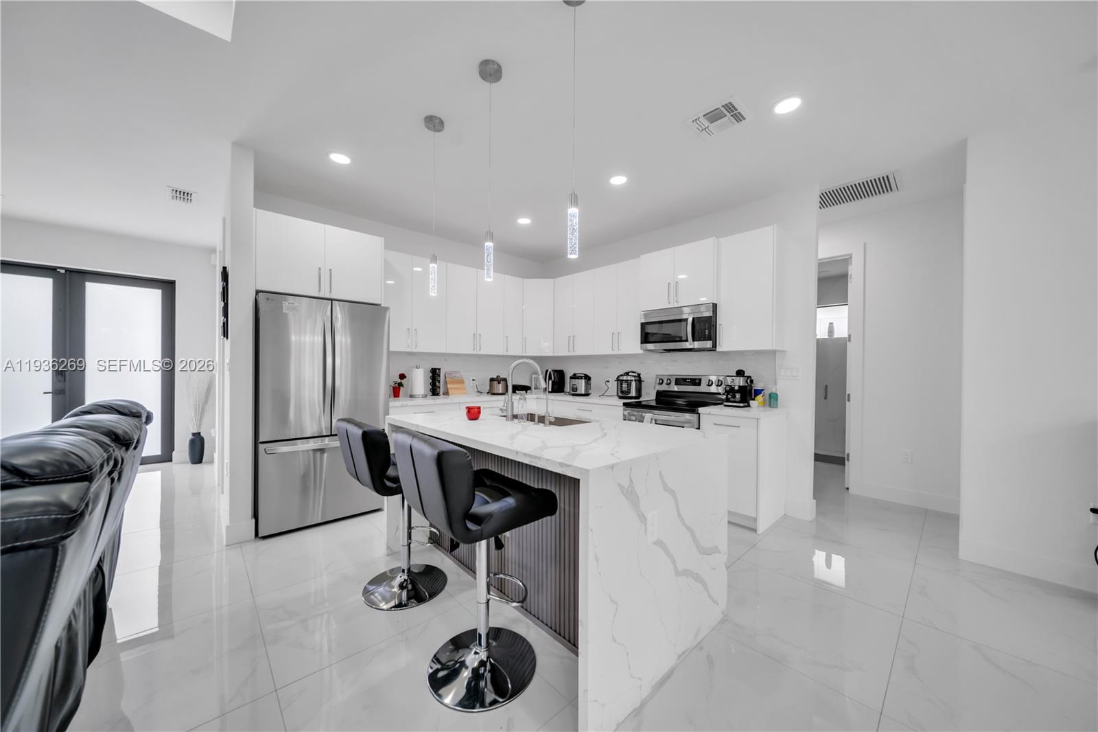 A modern kitchen features white cabinetry, a marble-topped island with bar stools, and stainless appliances — 1112 Clark Ave, Lehigh Acres FL 33972, LEHIGH ACRES, FL