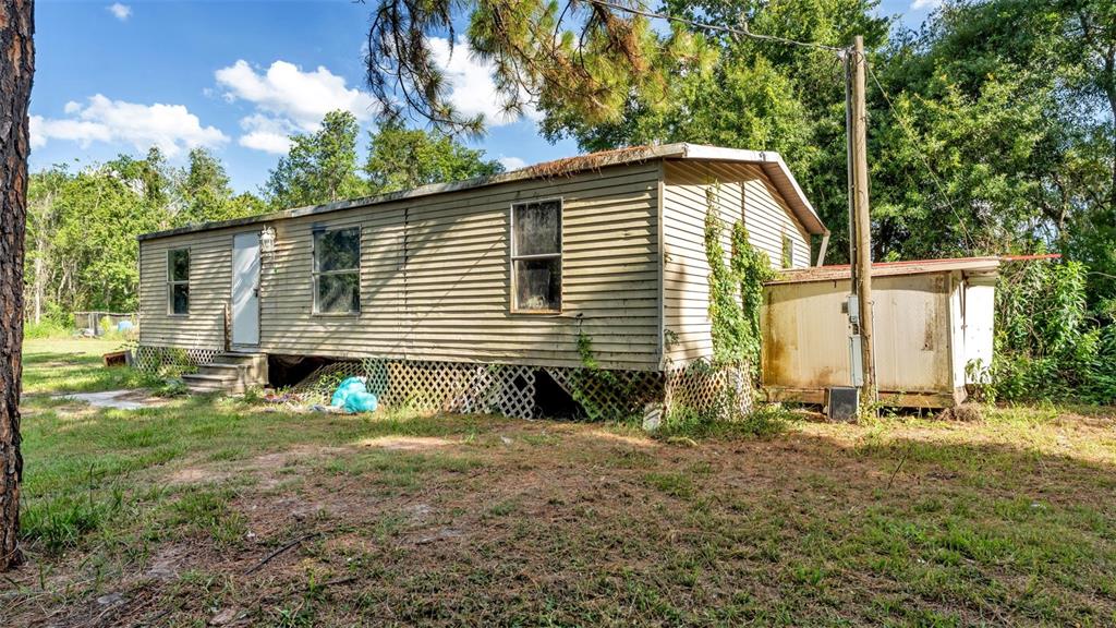 A single-story mobile home with tan siding and lattice skirting sits on a grassy lot — 2220 ELLIE ROAD UNIT B, AUBURNDALE, FL