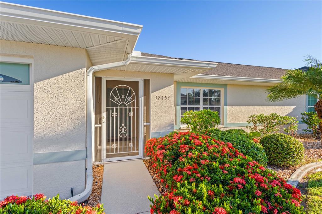 A single-story house exterior features a white screen door, a concrete walkway, and red flowers — 12454 SW KINGSWAY CIRCLE UNIT 202, LAKE SUZY, FL