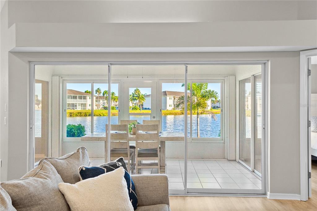 A living room looks through sliding glass doors to a dining area overlooking a lake — 12454 SW KINGSWAY CIRCLE UNIT 202, LAKE SUZY, FL