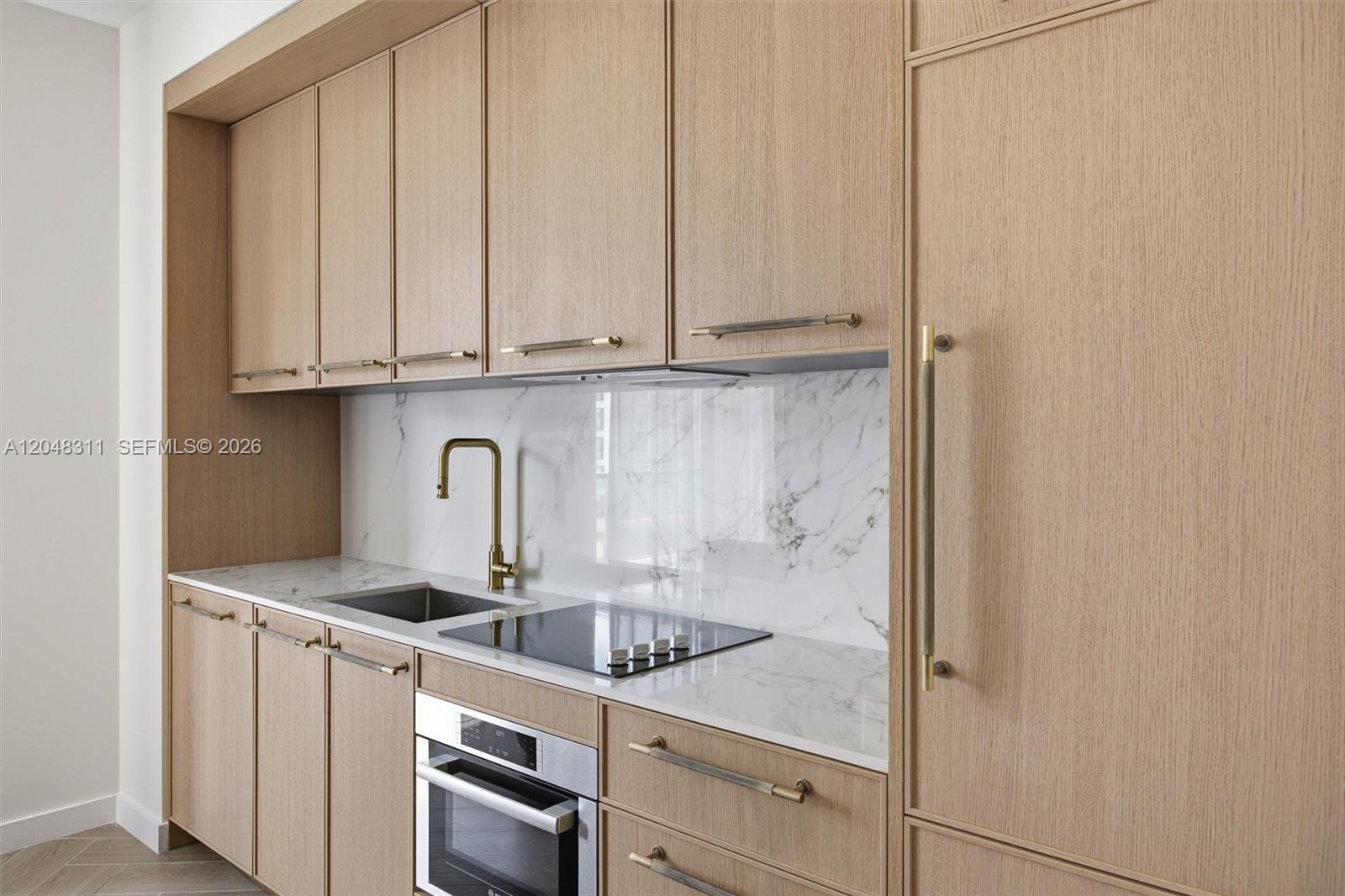 A modern kitchen features light wood cabinetry, a marble backsplash, and integrated stainless steel appliances — 2700 NW 2nd Ave # 432, Miami FL 33127, MIAMI, FL