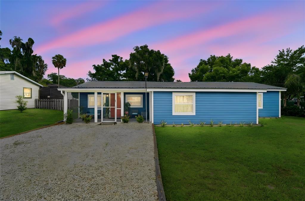 A blue single-story house with a gravel driveway and a screened-in front porch at sunset — 471 PINEGROVE STREET, DELAND, FL