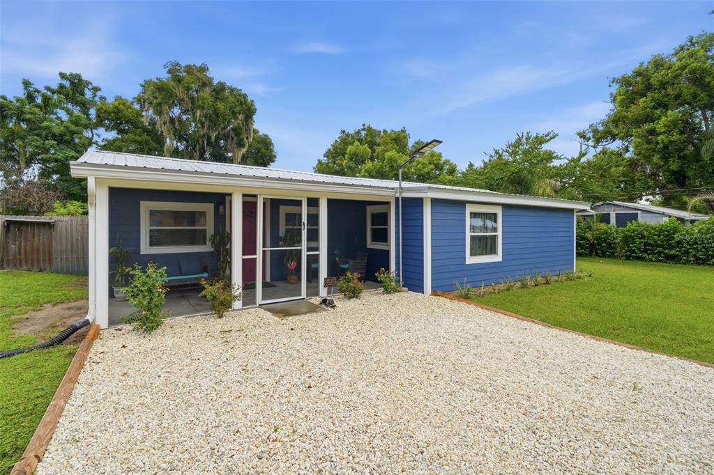 A blue single-story house features a white metal roof, a gravel driveway, and a screened porch — 471 PINEGROVE STREET, DELAND, FL