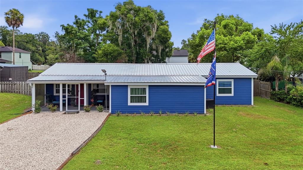A blue single-story house with a metal roof, a gravel driveway, and a flag pole — 471 PINEGROVE STREET, DELAND, FL