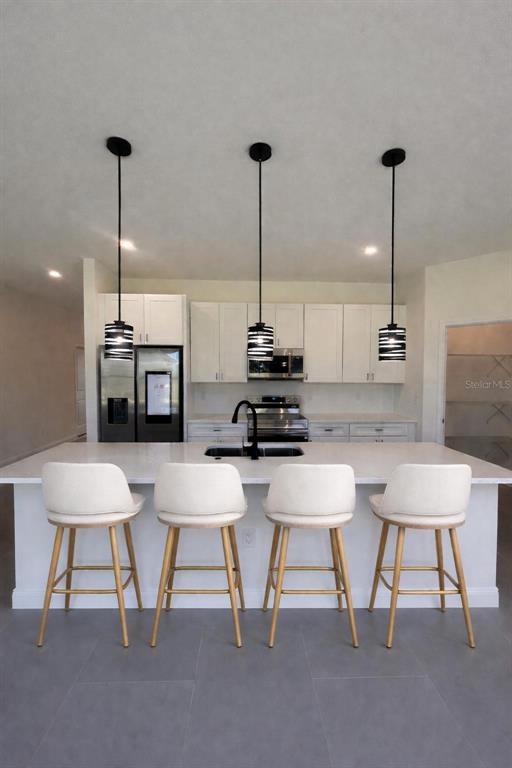 A kitchen features a white island with four bar stools and three hanging pendant lights — 4018 3RD STREET W, LEHIGH ACRES, FL