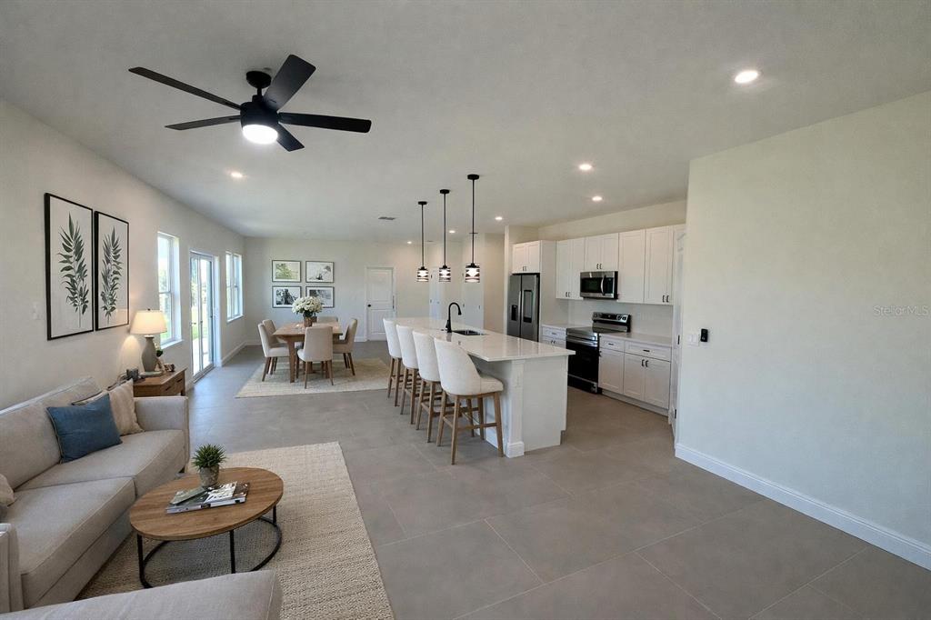 An open-concept living room and kitchen featuring white cabinetry, a large island, and tile flooring — 4018 3RD STREET W, LEHIGH ACRES, FL