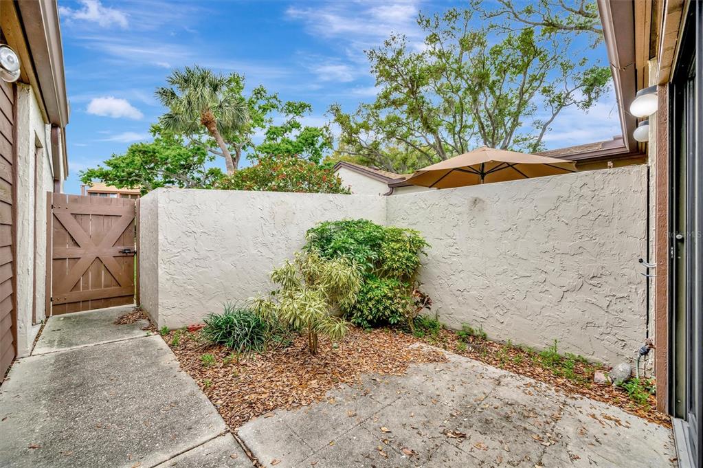 A concrete patio enclosed by a stucco wall with a wooden gate and landscaping — 2925 PARK LAKE DRIVE UNIT 12, BRADENTON, FL