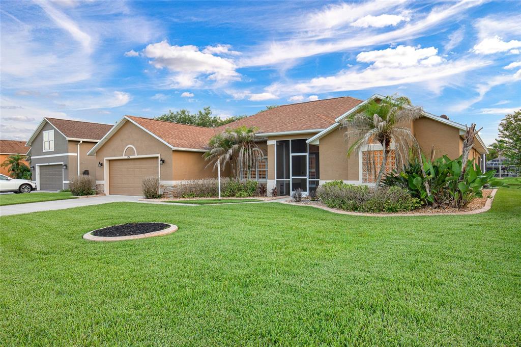 A tan single-story house with a two-car garage, a screened entryway, and a grassy lawn — 1714 CREEKWATER BOULEVARD, PORT ORANGE, FL