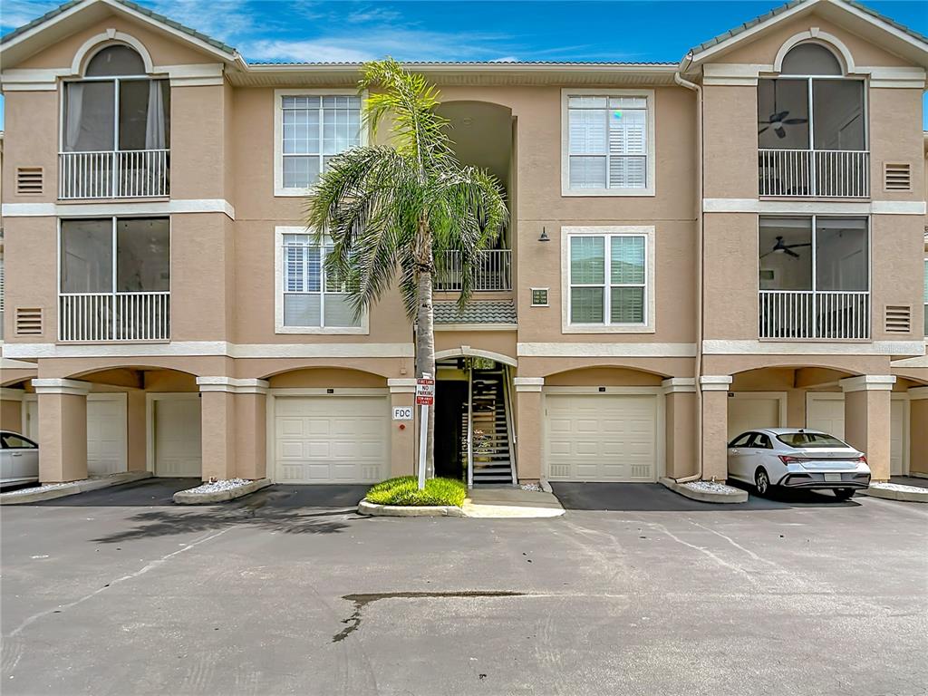 A three-story apartment building with tan stucco walls, two garages, and a central palm tree — 5308 BAY CLUB CIRCLE UNIT 5308, TAMPA, FL