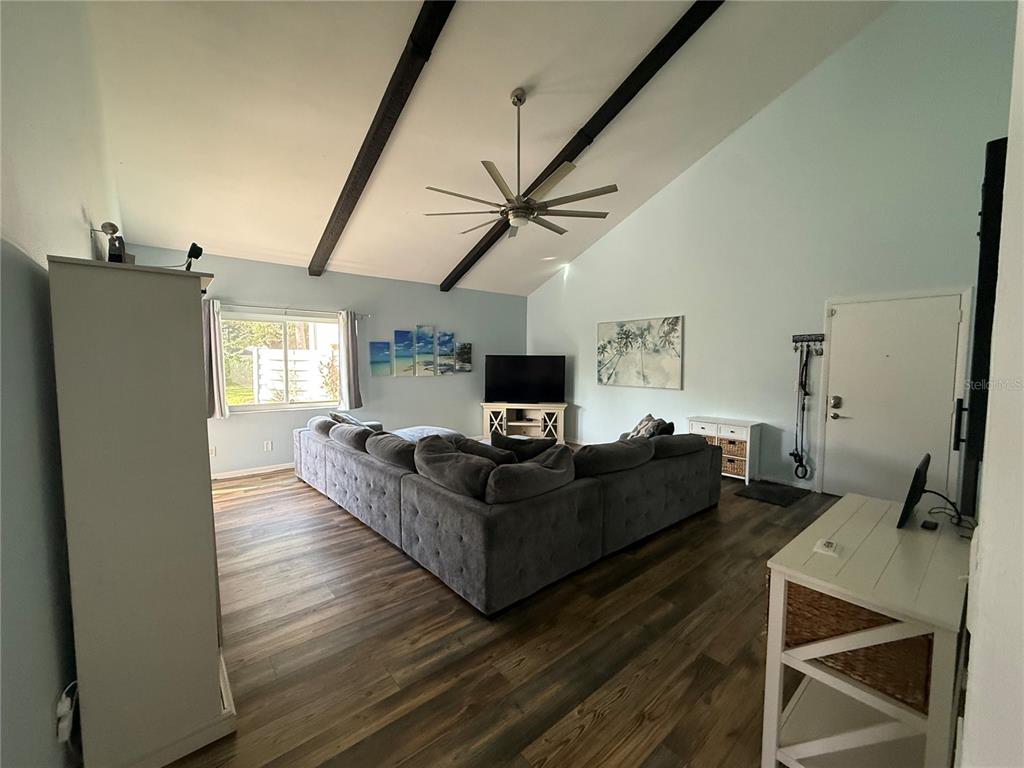 A living room features a large gray sectional sofa, vaulted ceilings with exposed beams, and wood-look flooring — 2641 CEDAR VIEW COURT, CLEARWATER, FL