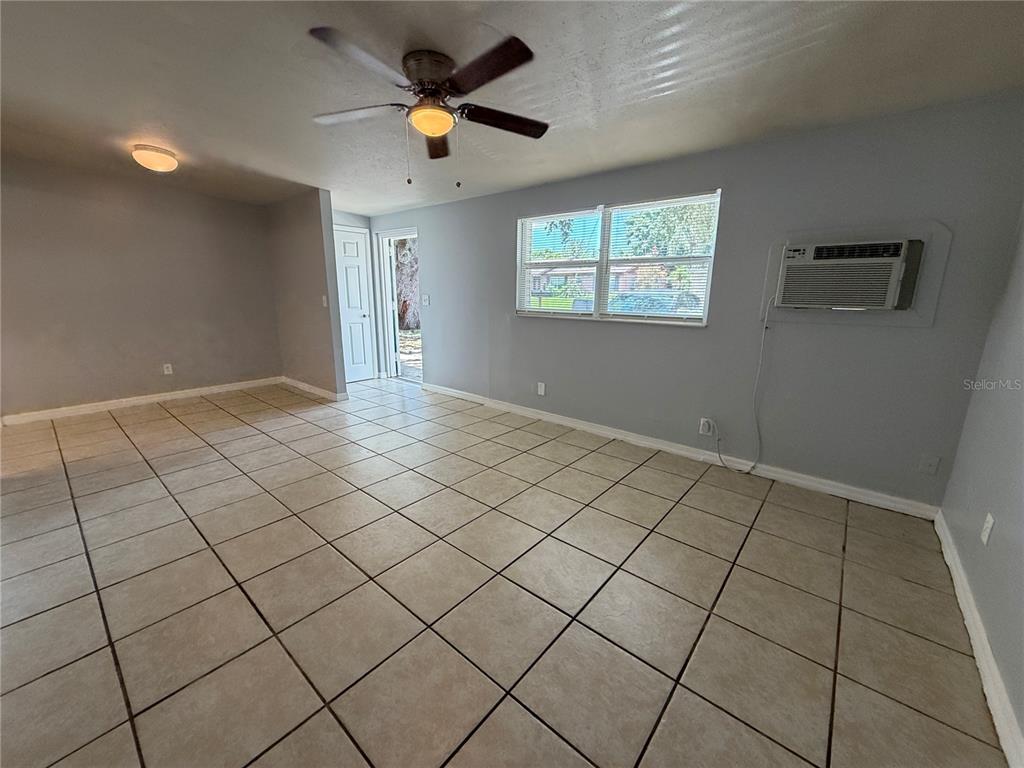 An empty room features light-colored tile flooring, gray walls, a ceiling fan, and a window unit — 2602 TRINITY CIRCLE NW UNIT B, WINTER HAVEN, FL