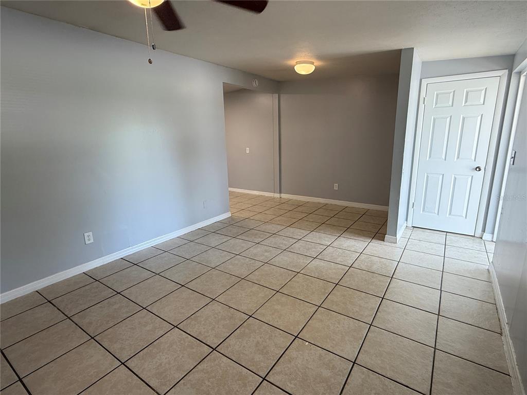 An empty room with light gray walls, tan tile flooring, and a white door — 2602 TRINITY CIRCLE NW UNIT B, WINTER HAVEN, FL