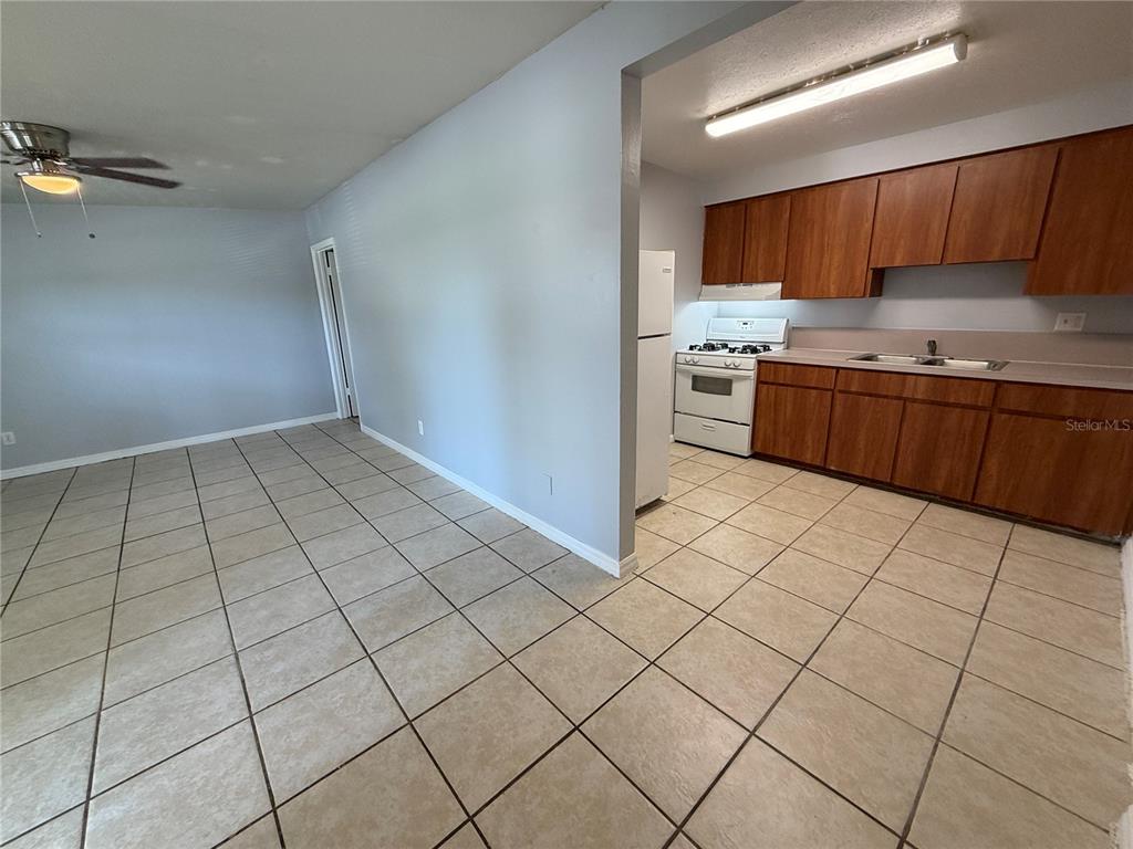 An open-concept kitchen with wood cabinets and tile flooring connects to a living area — 2602 TRINITY CIRCLE NW UNIT B, WINTER HAVEN, FL
