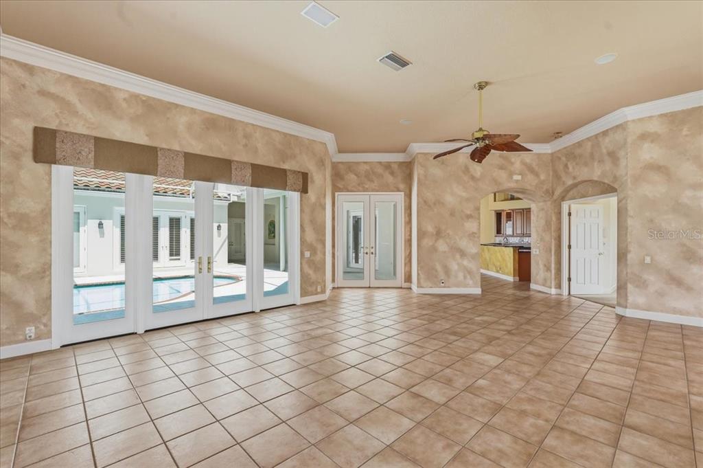 A spacious living room features tan faux-finish walls, tile flooring, and glass doors to a pool — 5221 88TH STREET E, BRADENTON, FL