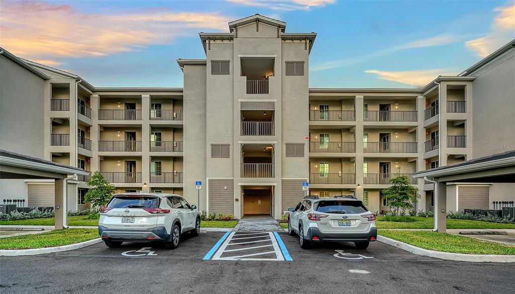 A multi-story apartment building exterior with two parked cars in front of accessible parking spaces — 17655 OPAL SAND DRIVE UNIT 301, VENICE, FL