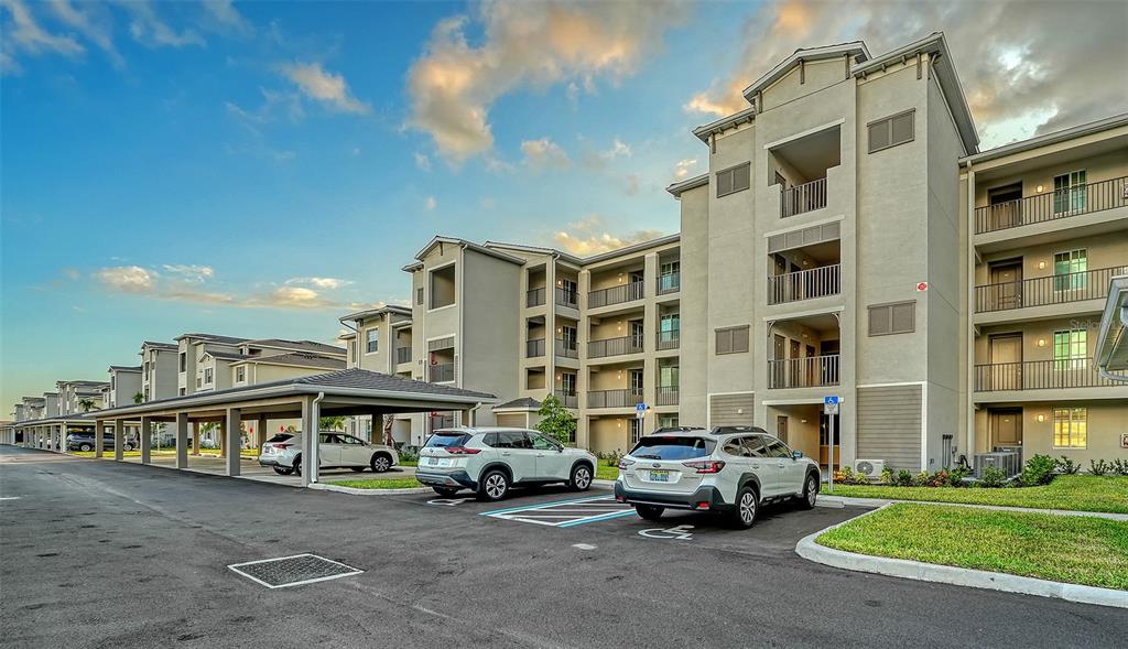 A multi-story apartment building with covered parking and parked cars in the foreground — 17655 OPAL SAND DRIVE UNIT 301, VENICE, FL
